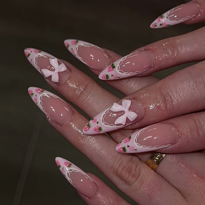 Kunstvolle Stiletto-Nägel mit floralen Akzenten und Schleifenverzierungen Brehn